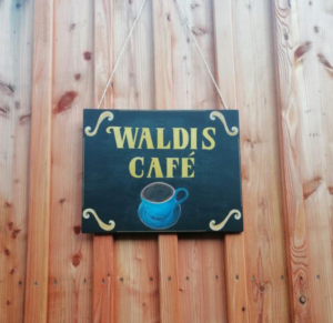 Eine hölzernde Bauwagen Wand mit einem Schild. Aufschrift des Schildes: "Wadlis Café"